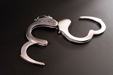 Pair of handcuffs used by law enforcement to arrest criminals on a black background. Justice or catching a guilty criminal concept.