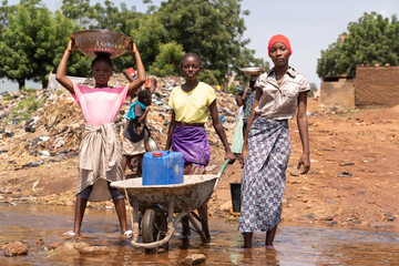 A group of young African village girls busy collecting drinking water with a wheelbarrow, water...