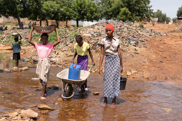 Group of African children transporting water supplies from the public well to their homes; lack of...