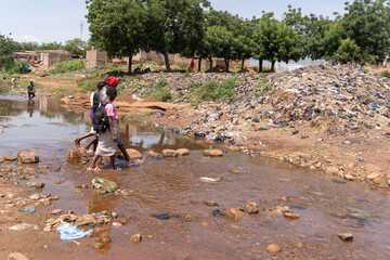 A group of African pupils forced to cross a flooded dirt road on their way to school after heavy...
