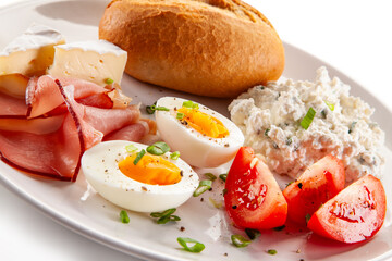 Continental breakfast - boiled eggs, white cheese, ham, tomatoes and bread roll on white background