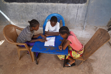 Group of West African schoolchildren learning lesson by sharing a single book - Concept of shortage...