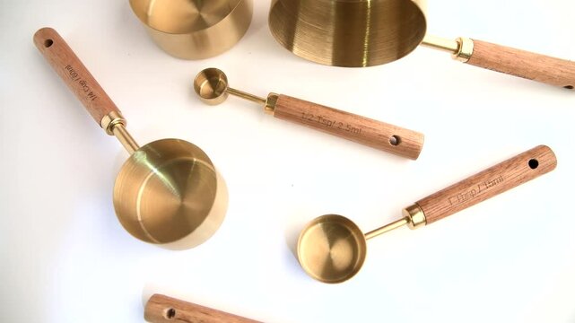 Copper measuring cups/spoons with a wooden handle in sets of different sizes on a white background.