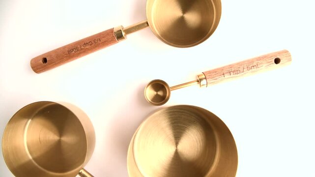 Copper measuring cups/spoons with a wooden handle in sets of different sizes on a white background.