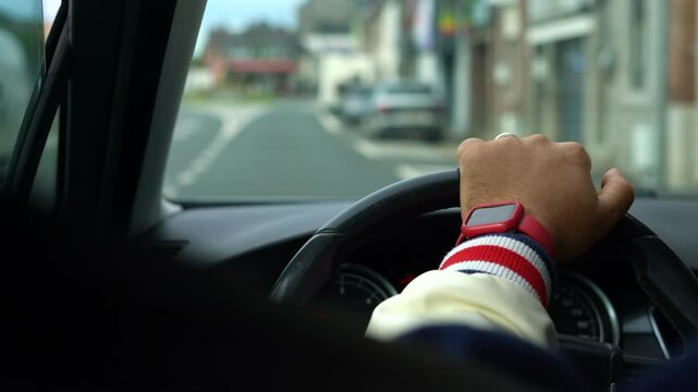 A closeup of a hand gripping a steering wheel while driving in the city