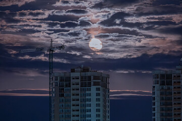 Night sky scene with partially obscured moon and under-construction modern buildings Contrasting...