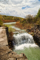 Spring day view of the old Welland Canal and lock walls. Water cascading over fallen rocks, stones of old canal lock. Overgrown river banks. Colorful trees, red, green, orange leaves.
