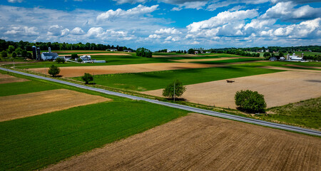Obraz premium Vast agricultural fields dominate the landscape, showcasing a mix of green crops and brown earth.