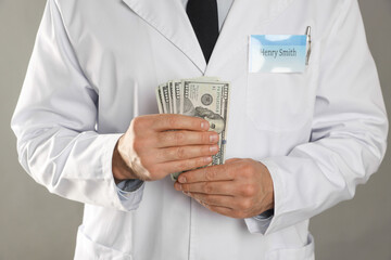 Corruption concept. Doctor with dollar banknotes on grey background, closeup