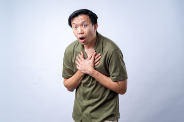 An Asian man in a casual green shirt clutches his chest with both hands, expressing pain or discomfort, standing against a clean white background. The image symbolizes chest pain