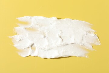 Cream on yellow background, closeup. Sample of cosmetic product