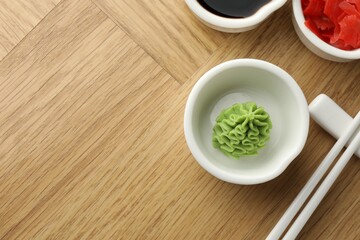 Hot wasabi paste, soy sauce, ginger and chopsticks on wooden table, flat lay. Space for text