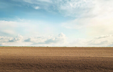 Expansive agricultural field under a cloudy sky near rural landscape in late afternoon