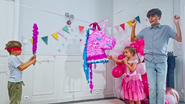 Joyful friends swings at a vibrant unicorn pinata on b-day party