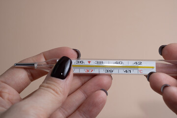 A close up image of a hand holding a traditional glass mercury thermometer with a visible temperature reading