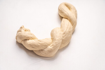 The dough is braided into a pigtail on a white background. The process of preparing baked goods