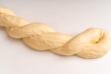 The dough is braided into a pigtail on a white background. The process of preparing baked goods
