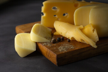 different types of cheese on wooden board on black background. Cheese product cut into pieces on cutting board