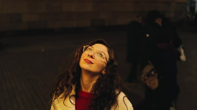 Magic Christmas, New Year, cinematic portrait of a curly-haired woman with glasses standing under garlands on the festive streets of the city, weekend, beauty, shine, sparkles, wish, winter, dreamy