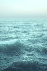 Fototapeta premium A serene view of gentle ocean waves under a soft, hazy sky, creating a calm and peaceful atmosphere.