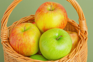 Green and red apples in a basket on a green background.