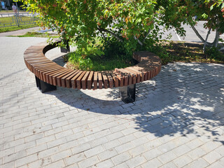 Semicircular wooden brown bench in the park on a bright sunny day