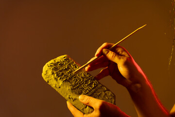 hands holding an Egyptian antiquity cuneiform clay tablet and writing ancient writings