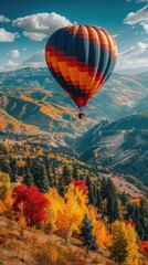 Naklejka premium A vibrant hot air balloon floats over a colorful autumn landscape with mountains in the background.