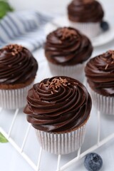 Tasty cupcakes with chocolate cream and blueberries on white tiled table, closeup
