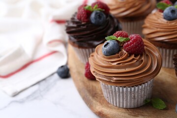 Tasty cupcakes with chocolate cream and berries on white marble table, closeup. Space for text