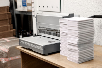 Modern binding machine and stacks of notebooks on wooden table indoors