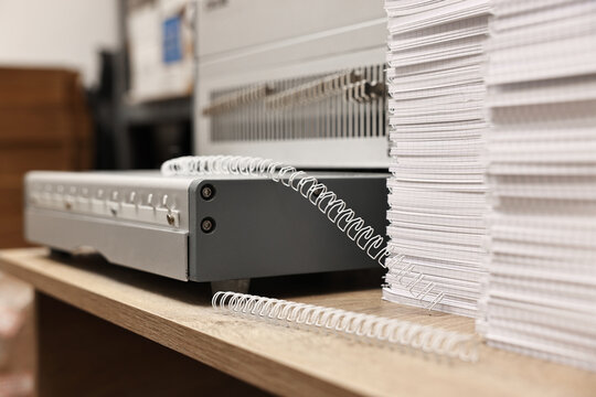 Modern binding machine, stacks of notebooks and double loop wire binding spines on wooden table indoors, closeup