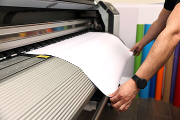 Man using wide-format printer indoors, closeup. Printing house