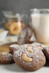 Tasty chocolate cookies with cashew and powdered sugar on white table, closeup