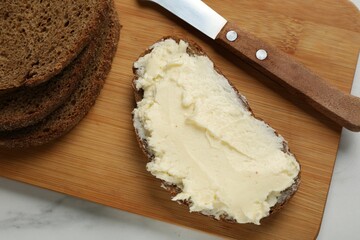 Fresh bread with butter and knife on white table, top view