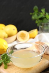 Fresh lemon juice in bowl and fruits on wooden table, closeup