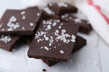 Pieces of chocolate with salt on white table, closeup