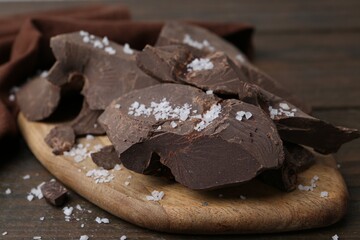 Pieces of chocolate with salt on wooden table, closeup