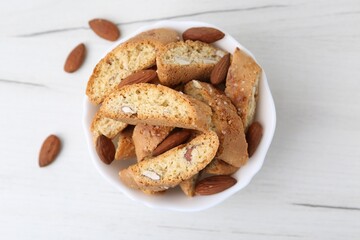 Tasty almond biscuits (Cantuccini) and nuts in bowl on white wooden table, top view