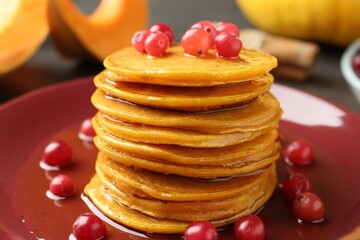 Tasty pumpkin pancakes with cranberries and honey on plate, closeup
