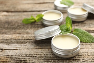 Natural lip balms and mint leaves on wooden background, selective focus. Space for text