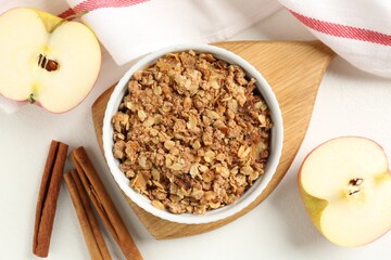 Delicious apple crisp in bowl, fresh fruits and cinnamon sticks on white table, flat lay
