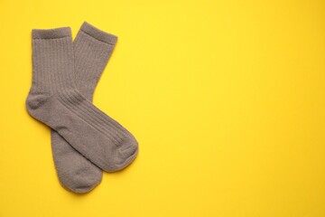 Pair of soft socks on yellow background, top view. Space for text