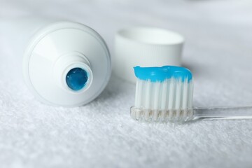 Toothbrush with toothpaste and tube on white towel, closeup