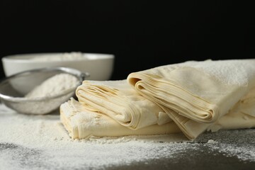 Raw puff pastry dough and flour on dark table against black background, closeup