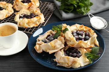 Tasty puff pastries with blueberries, powdered sugar, mint and coffee on dark table, closeup