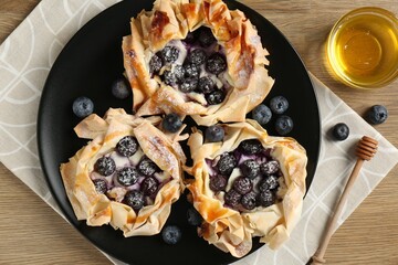 Tasty puff pastries with blueberries and honey on wooden table, top view