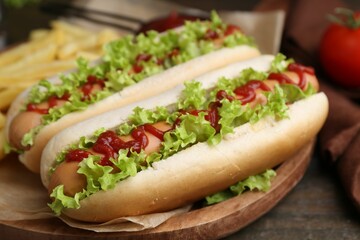 Tasty hot dogs with lettuce, ketchup and potato fries on wooden table, closeup