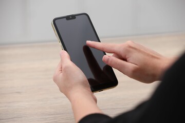 Woman using smartphone with blank screen at wooden table, closeup