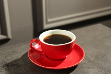 Red cup of aromatic coffee and saucer on dark textured table, closeup